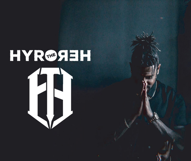 shapers-club- Un homme aux cheveux tressés et tatoué se tient debout, les mains jointes en signe de prière. À côté de lui figurent les mots « HYRO THE HERO », un logo stylisé « HTH » et un clin d'œil subtil au Shapers Club sur un fond sombre. -surf