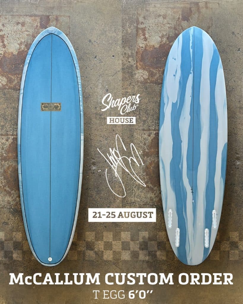 shapers-club- Deux planches de surf bleues présentées côte à côte sur du béton, portant les inscriptions Sur-mesure "Shapers Club House", "21-25 August" et Jeff McCallum Custom Order. Le texte superposé comprend "T Egg 6'0" avec une signature blanche présente. -surf